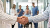 Close up of doctor and shaking hands with other care professionals and a patient in the background